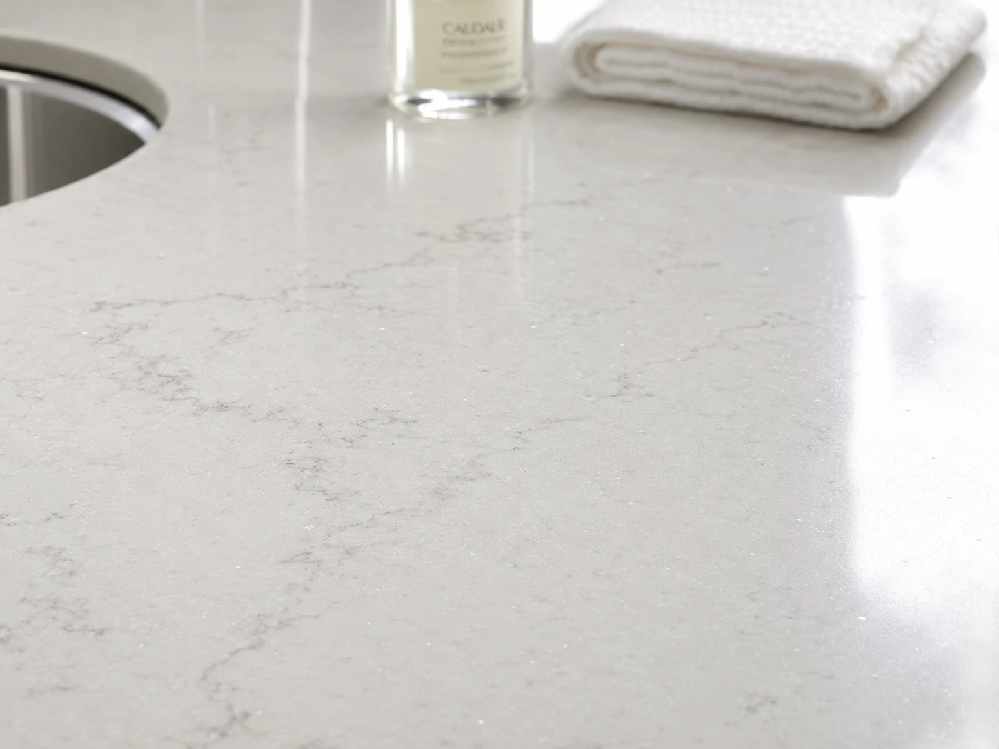 Close-up of polished white quartz bathroom vanity top with subtle grey veining and undermount basin Close-up of polished white quartz bathroom vanity top with subtle grey veining and undermount basin