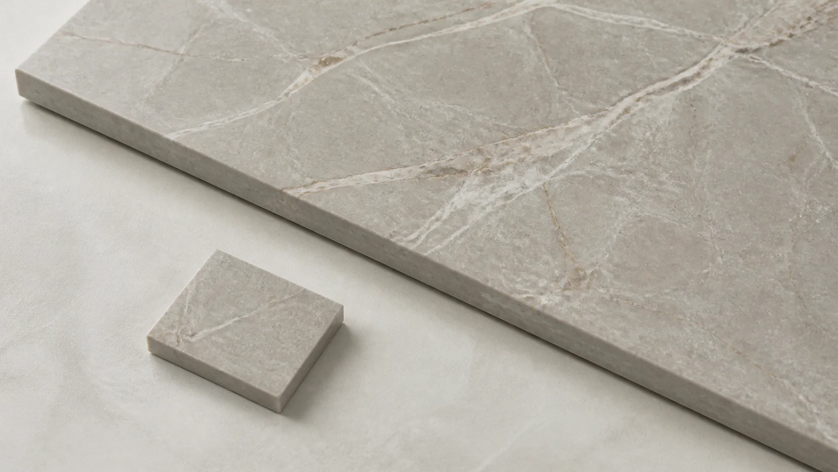 Small countertop sample chip held beside a full stone slab showing the size and veining difference