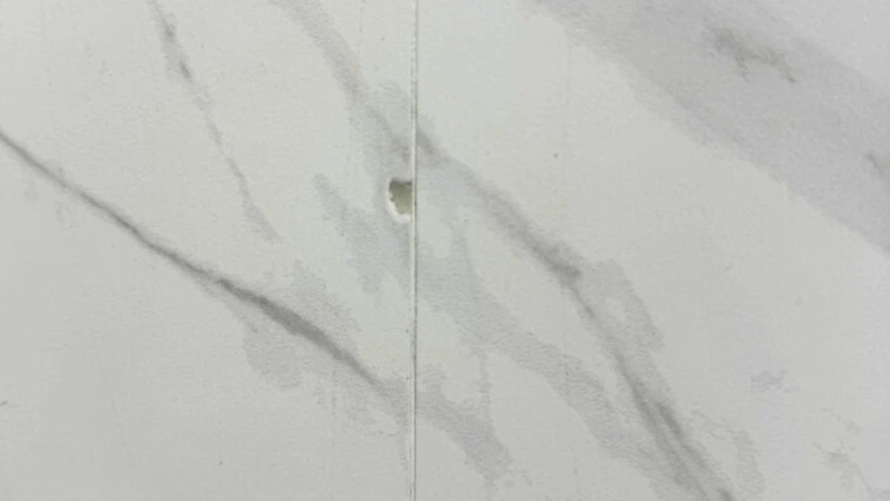 Close-up of chipped edge on a porcelain countertop showing exposed white body beneath dark veined surface