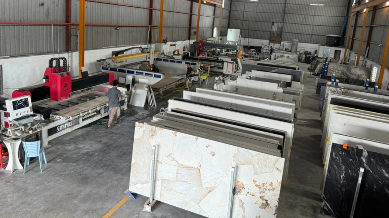 Bridge saw machine cutting through a white quartz stone slab with water spray in a fabrication workshop