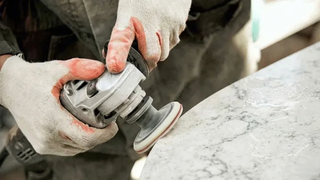 Worker polishing the chamfered edge of a sintered stone countertop piece using a hand polisher in fabrication workshop