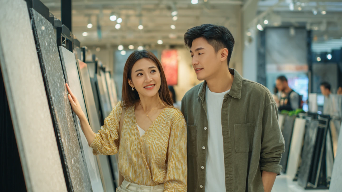 Malaysian homeowner couple examining sintered stone and quartz countertop samples in a stone showroom, considering their kitchen renovation options Malaysian homeowner couple examining sintered stone and quartz countertop samples in a stone showroom, considering their kitchen renovation options