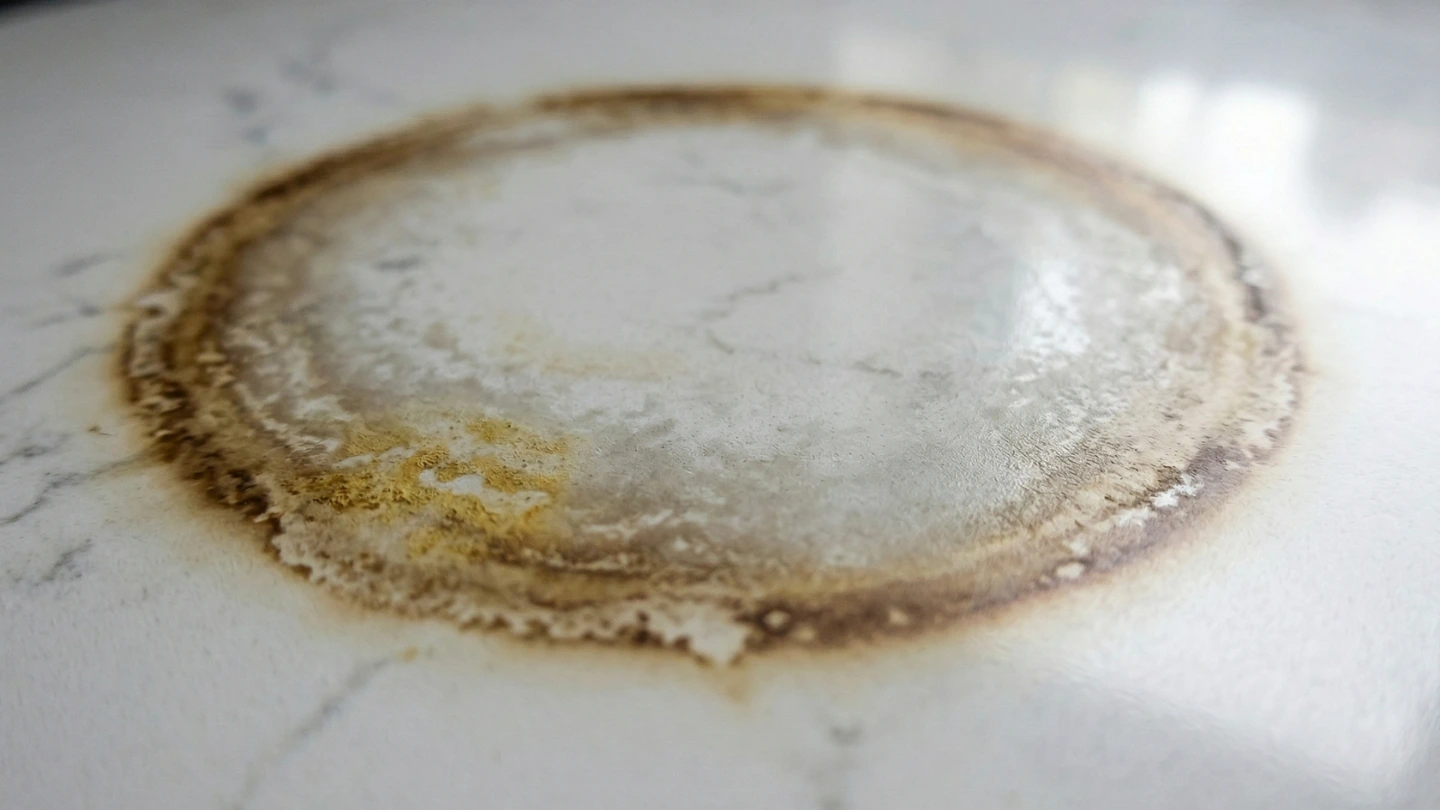 Close-up of heat damage on a white quartz stone countertop showing a visible circular scorch mark and discolouration caused by placing a hot pan directly on the surface Close-up of heat damage on a white quartz stone countertop showing a visible circular scorch mark and discolouration caused by placing a hot pan directly on the surface